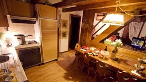 A kitchen with wooden cabinets, a dining table with chairs, and a hanging light fixture. - San Vito: Beautiful apartment a stone's throw from Cortina d 'Ampezzo (San Vito di Cadore)