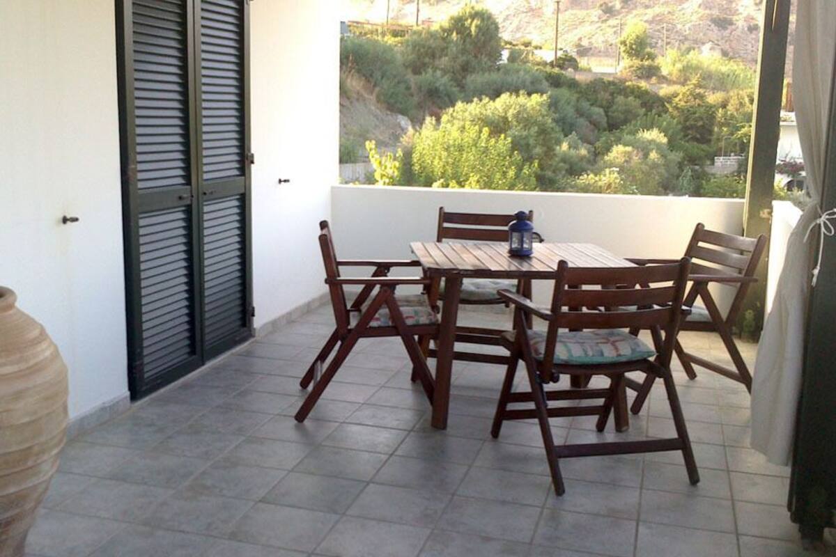 Ein Balkon mit Holztisch und Stühlen, einer großen Vase und Blick auf Grünflächen.
