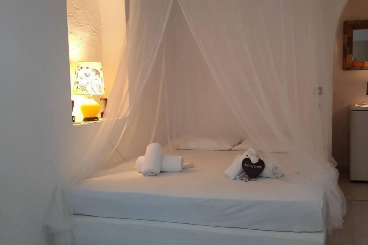 Ein ordentlich bezogenes Bett mit Baldachin, ein Nachttisch mit Lampe und ein kleiner Kühlschrank.