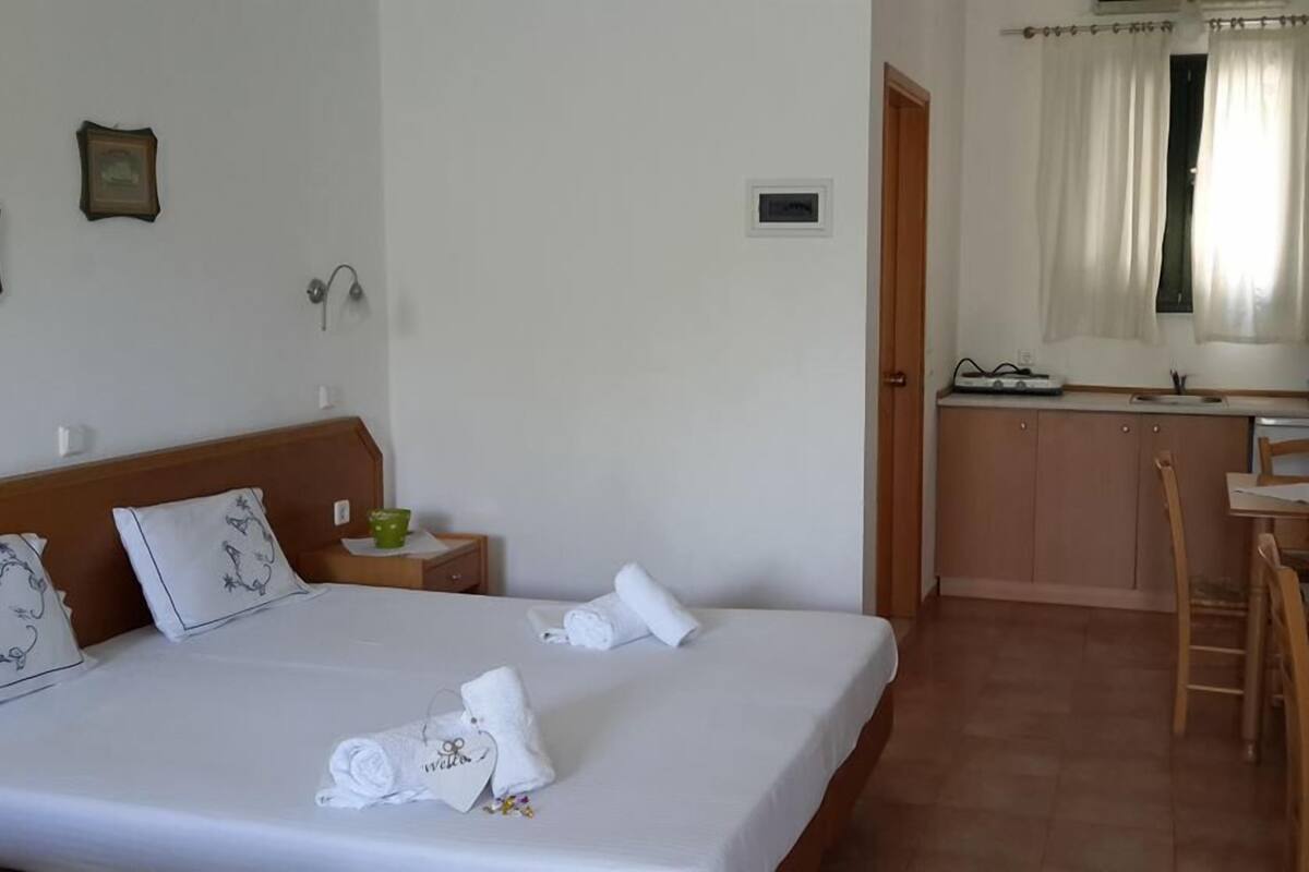 Ein Hotelzimmer mit einem Bett, einem kleinen Nachttisch, einem Holzstuhl, einer Küchenzeile und einer Badezimmertür.
