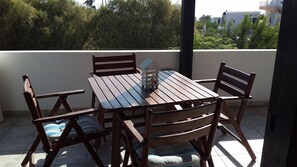 Et træbord og stole på en balkon med udsigt til bygninger og træer.