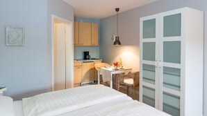Un dormitorio con cama, escritorio con silla, kitchenette y armario con puertas de vidrio esmerilado.