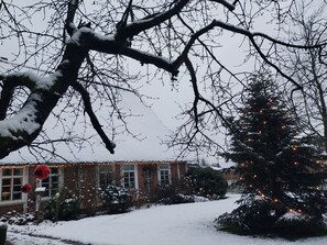 A snow-covered landscape with bare trees and a brick building with windows.