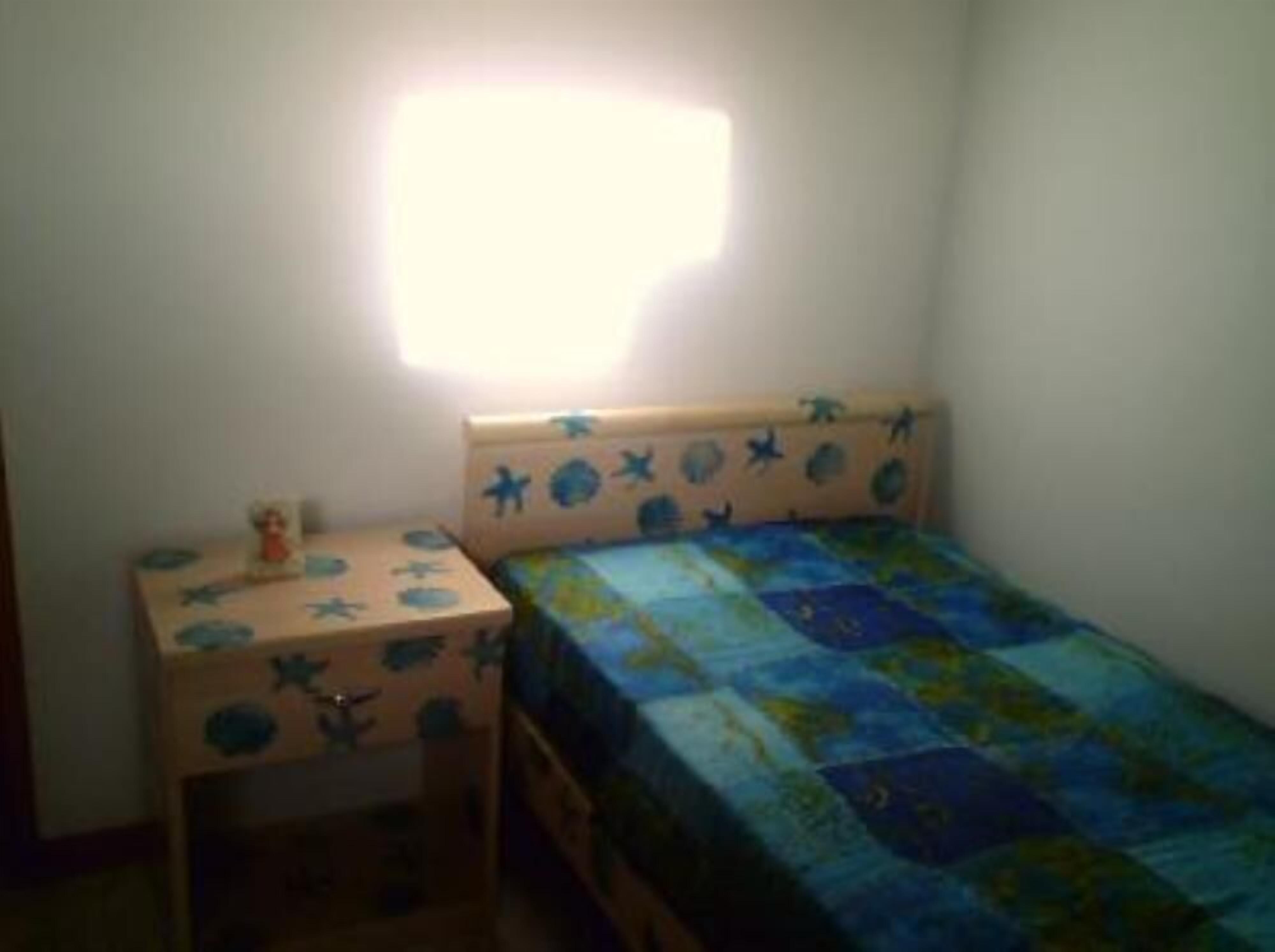 A small, single-bed room with a wooden headboard, a bedside table, and a nightstand.