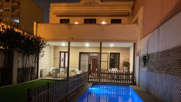 Una piscina con cubierta de madera y cerramiento, rodeada por un edificio con un cartel.