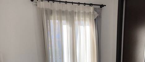 A room with a bed, a wooden floor, a black wardrobe, and sheer curtains.