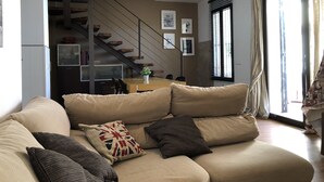 Una sala de estar con un sofá color beige, una escalera y un comedor.