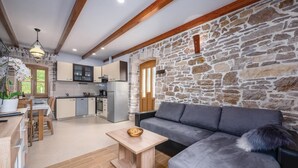 A modern kitchen with stone walls, a dining area with a sofa, and a wooden table. - Lovely home in Medancici (Medancici)