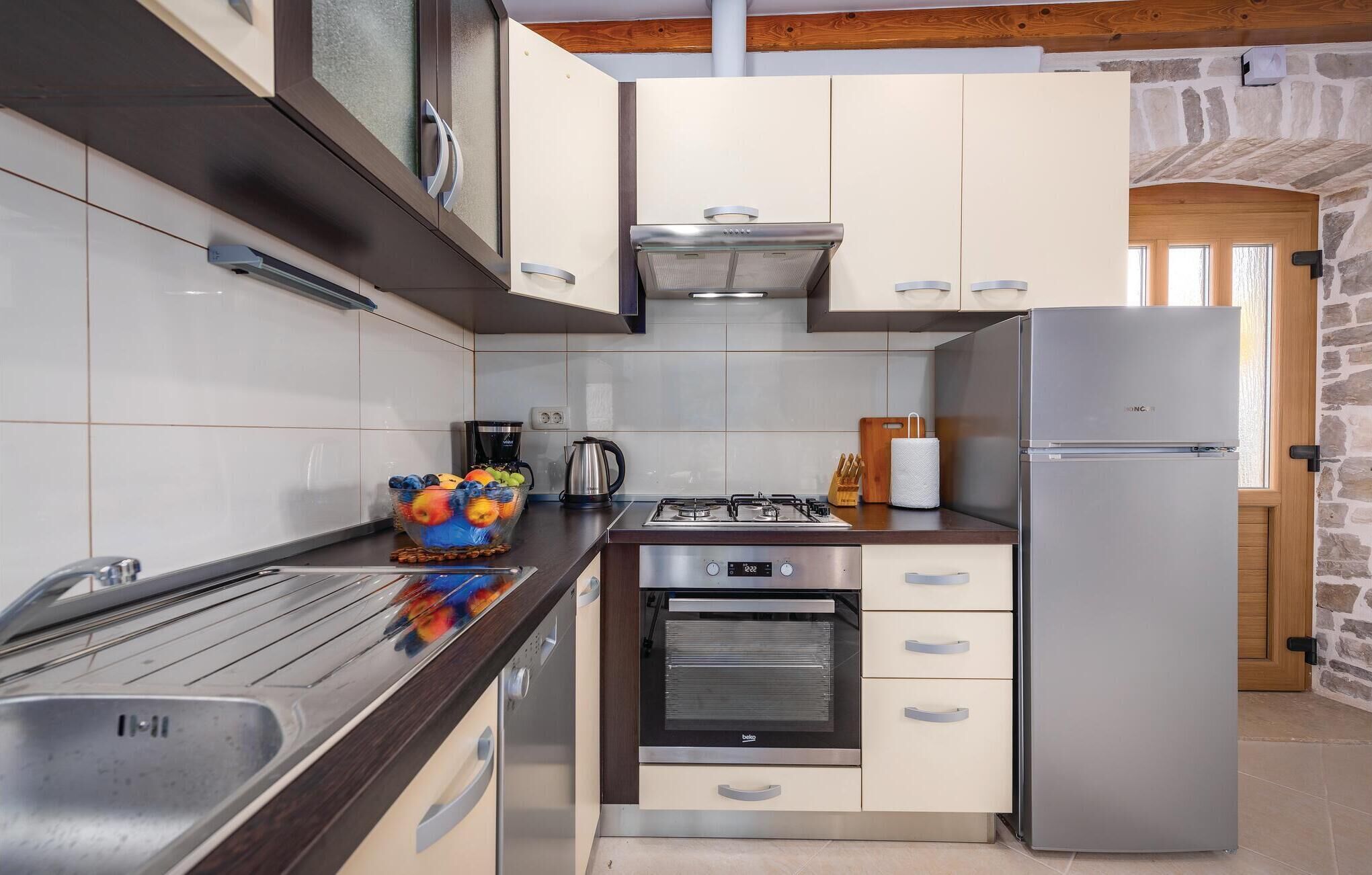 A modern kitchen with a gas stove, oven, stainless steel refrigerator, and a bowl of fruit on the counter.