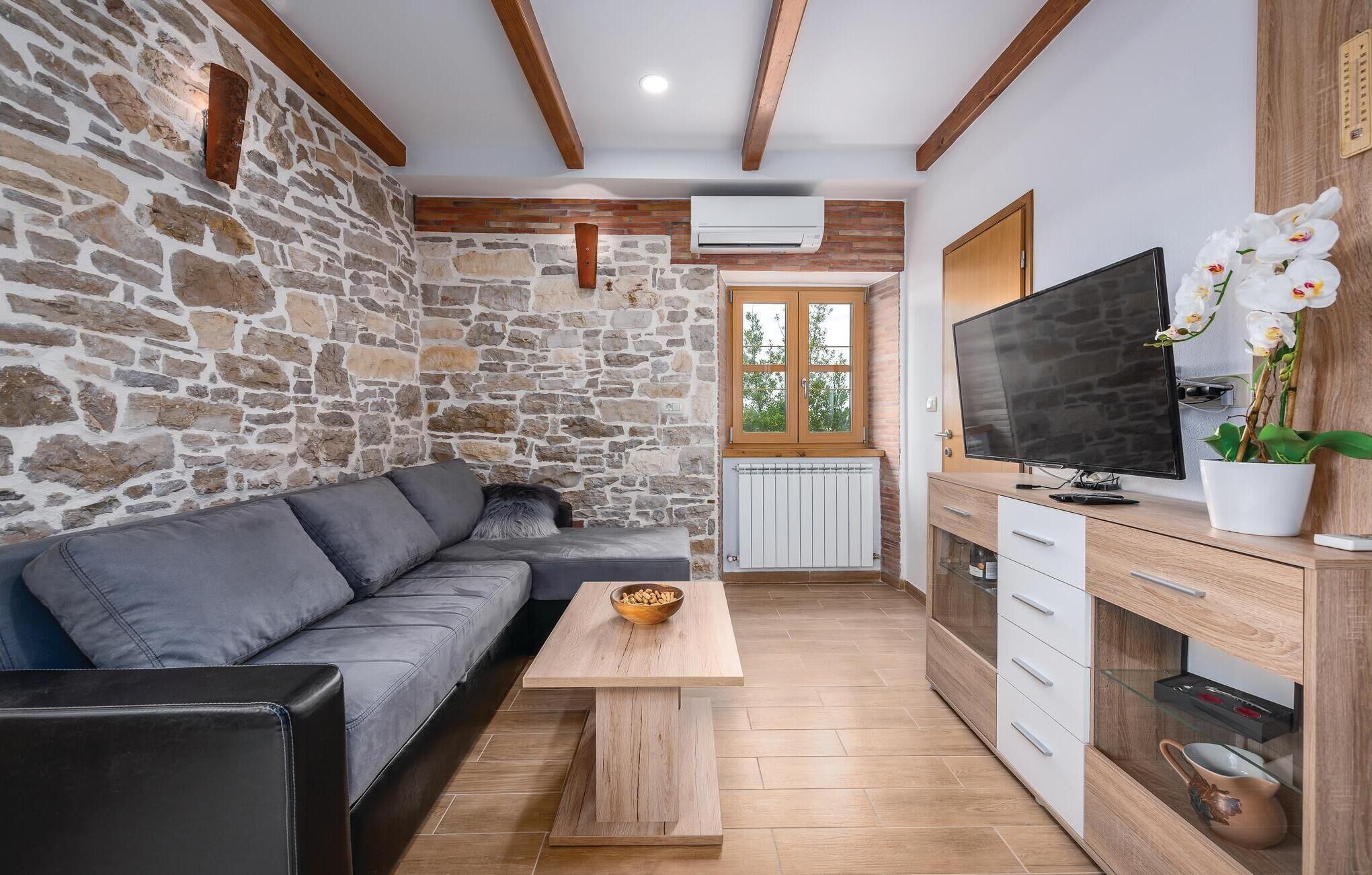Un salon moderne avec un mur en pierre, un canapé gris, une table basse en bois, un téléviseur et un meuble avec des tiroirs.