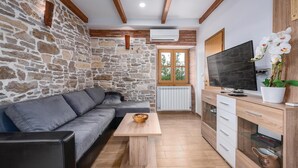 A modern living room with a stone wall, a grey sofa, a wooden coffee table, a TV, and a cabinet with drawers. - Lovely home in Medancici (Medancici)