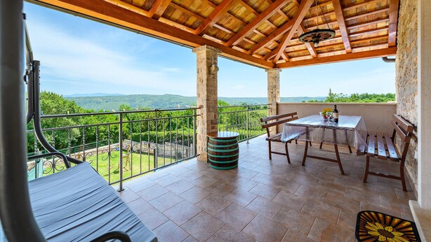 A covered patio with a table and chairs, a wooden ceiling, and a view of green hills. - Lovely home in Medancici (Medancici)