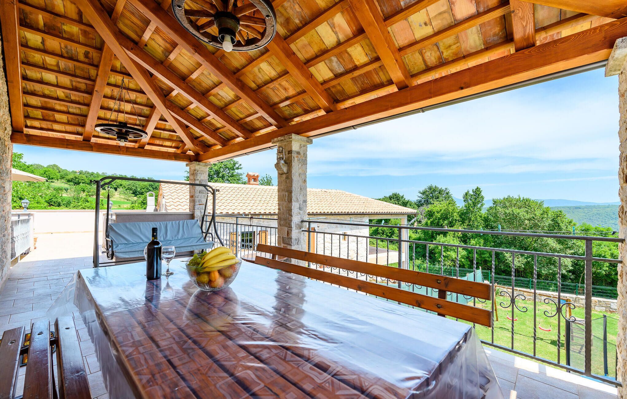Eine Terrasse im Freien mit einem Holztisch, einer Bank und Blick auf die Landschaft.