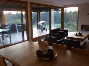 Ein modernes Wohnzimmer mit einem Holzesstisch, einem Kamin und Blick auf eine Terrasse und Außenbereich.