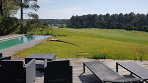 Zona junto a la piscina con sillones de descanso y vista a un río y bosque.