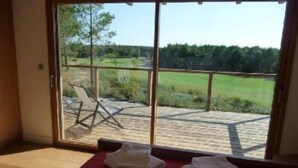 Habitación con un amplio ventanal corredero que da a una terraza exterior con vistas a un campo verde y árboles.