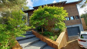 Una casa moderna con una escalera de madera que lleva a un porche cubierto, rodeada de abundante vegetación.