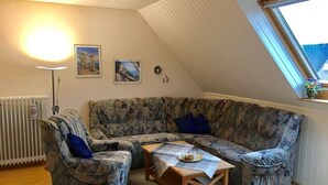 A cozy living room with a sectional sofa, a wooden coffee table, and a radiator. - Quiet upper apartment in the middle of Norddeich for 4 people + baby (Norden)