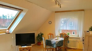 A dining area with a table, chairs, a television, and a window with a view of a brick building. - Quiet upper apartment in the middle of Norddeich for 4 people + baby (Norden)