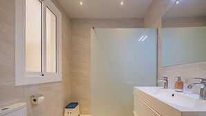 Un baño moderno con inodoro, cabina de ducha, lavabo con espejo y un pequeño taburete.