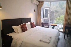 A hotel room with a large bed, a small table, a chair, and a window with curtains. - Qingcheng Country Villa (Dujiangyan)