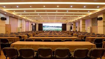 A conference room with rows of tables and chairs, a large screen at the front, and a projector.