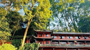 A traditional building with multiple levels and a red exterior, surrounded by lush greenery and tall trees.