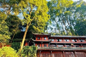 Un edificio tradicional de varios niveles y fachada roja, rodeado de abundante vegetación y altos árboles.