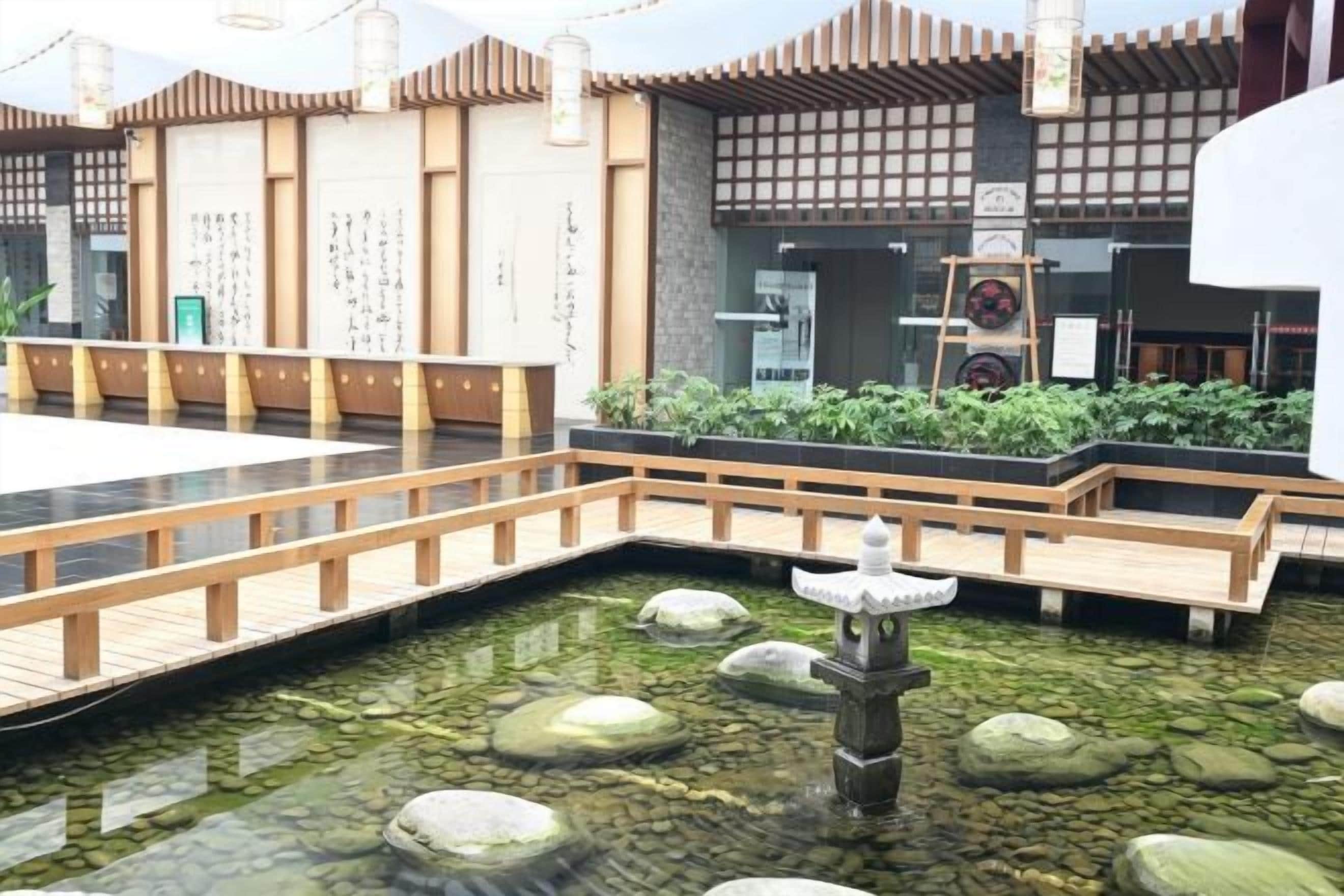 Un patio tradicional japonés con un puente de madera, un estanque de carpas y un farol de piedra.
