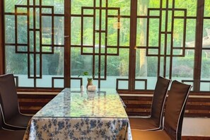 A dining area with a table and chairs, a decorative screen, and a view of greenery. - Qingcheng Country Villa (Dujiangyan)