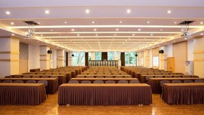 Egy konferenciaterem, sorokban elrendezett asztalokkal, projektorral és egy színpaddal.