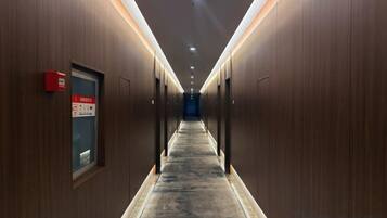Corredor de hotel com paredes de madeira, piso coberto de carpete e placa de saída de emergência vermelha.