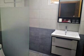 Un baño con cabina de ducha de vidrio, un lavamanos blanco con espejo encima y una pared de color oscuro.