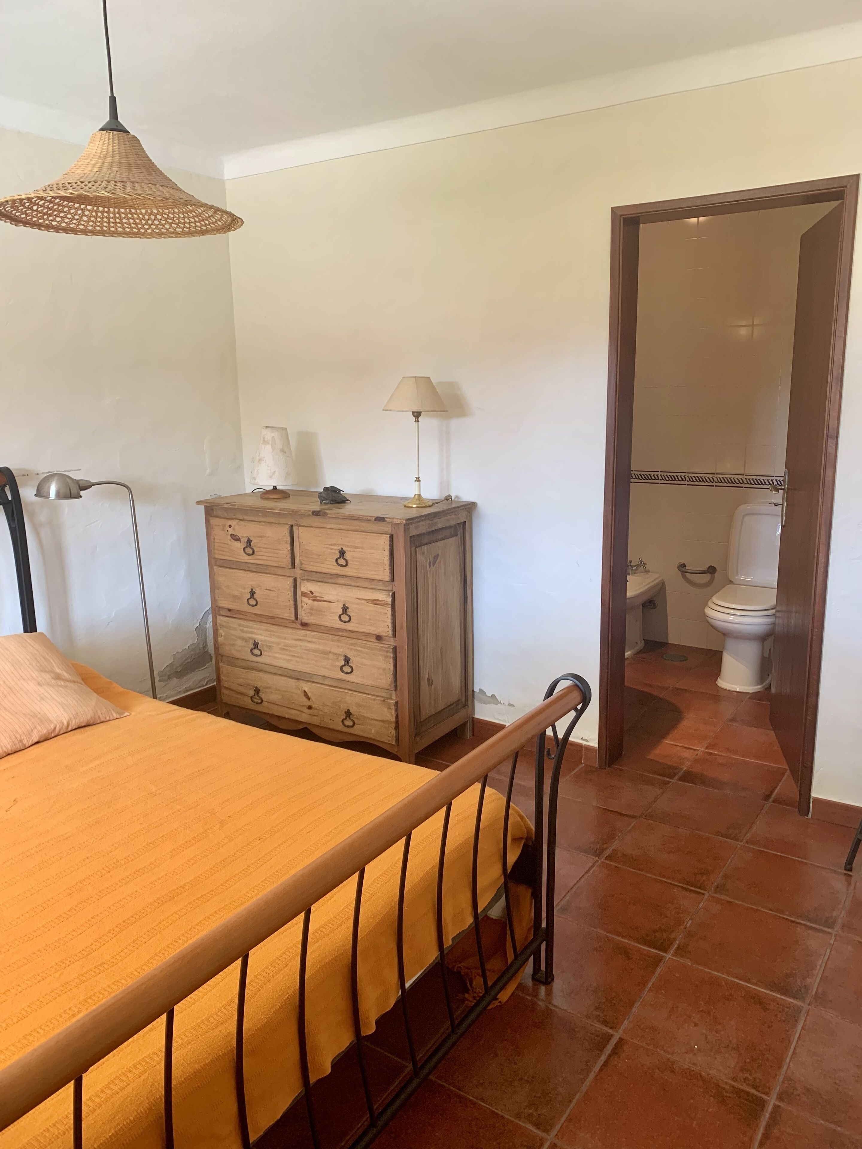 Een slaapkamer met een bed, een houten dressoir, een lamp en een badkamer die door een geopende deur zichtbaar is.