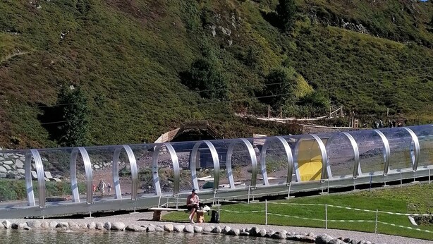 A clear water body with people in inflatable boats, a metal bridge, and a hilly landscape in the background. - New, stylish top floor apartement, free Wifi, bus stop directly at the house (Ramsau im Zillertal)
