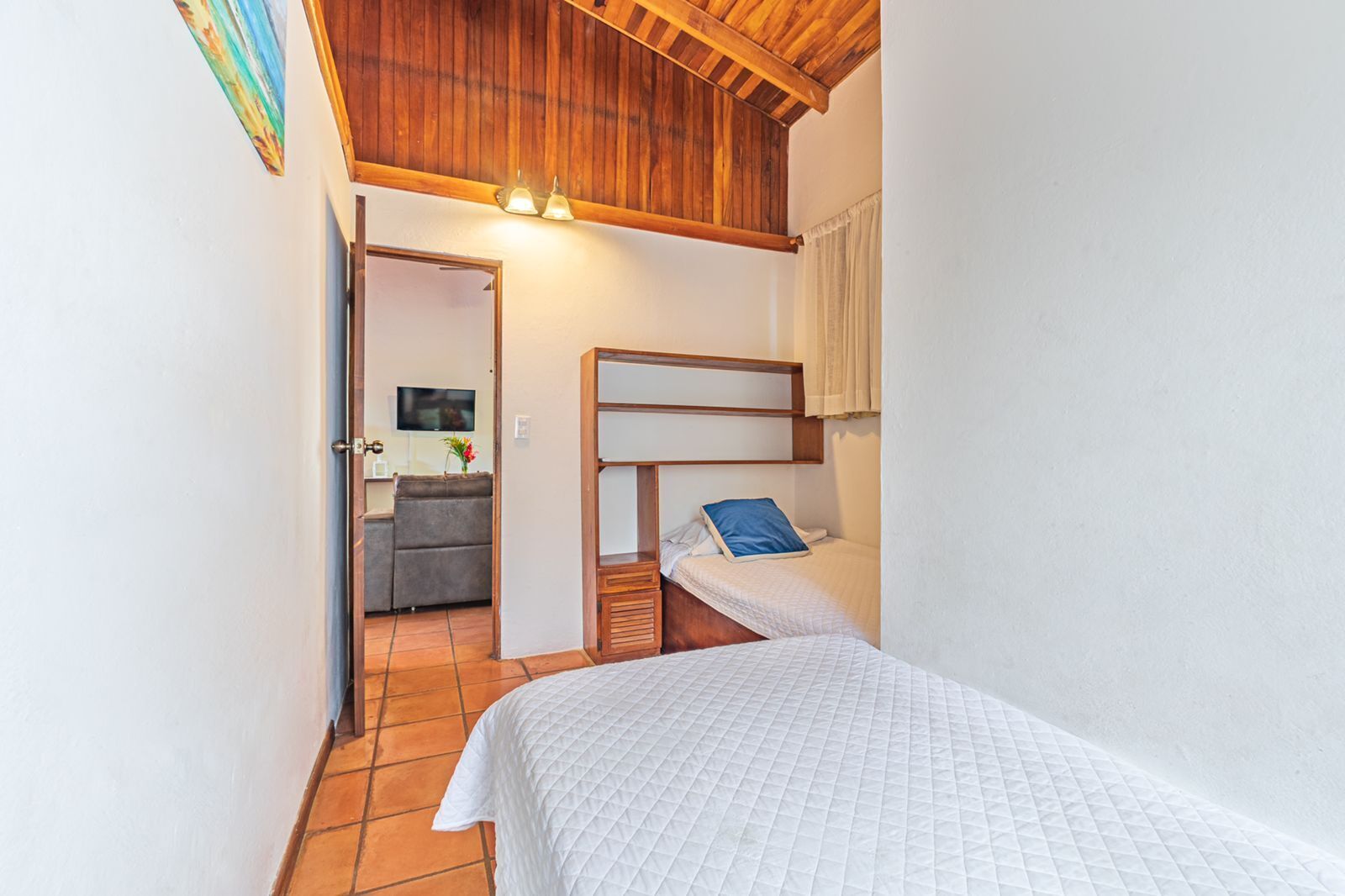 Una camera da letto accogliente e piccola con soffitto in legno, un letto singolo con cuscino blu e una scrivania con sedia.