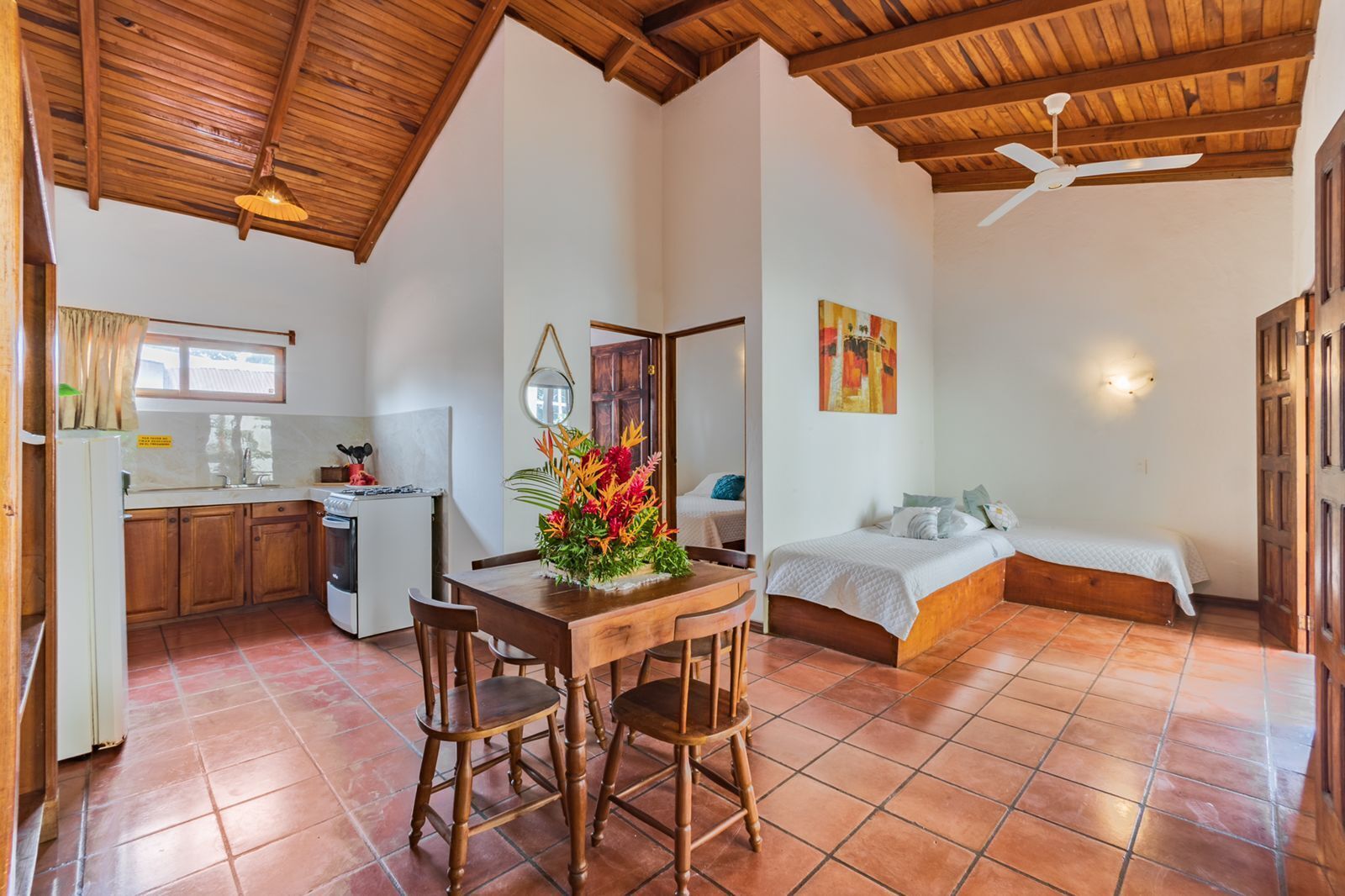 A compact room with a bed, a dining table with chairs, a kitchen area, and a ceiling fan.