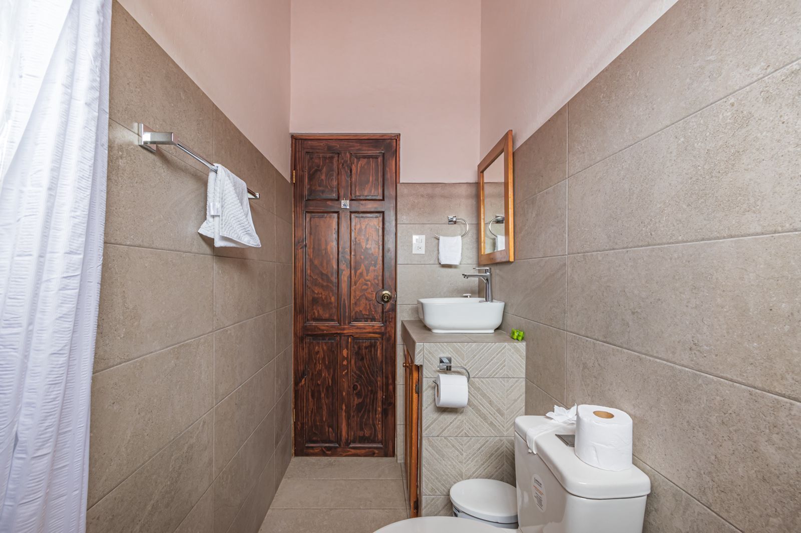 A narrow bathroom with a wooden door, a white sink, a toilet, and a towel rack.