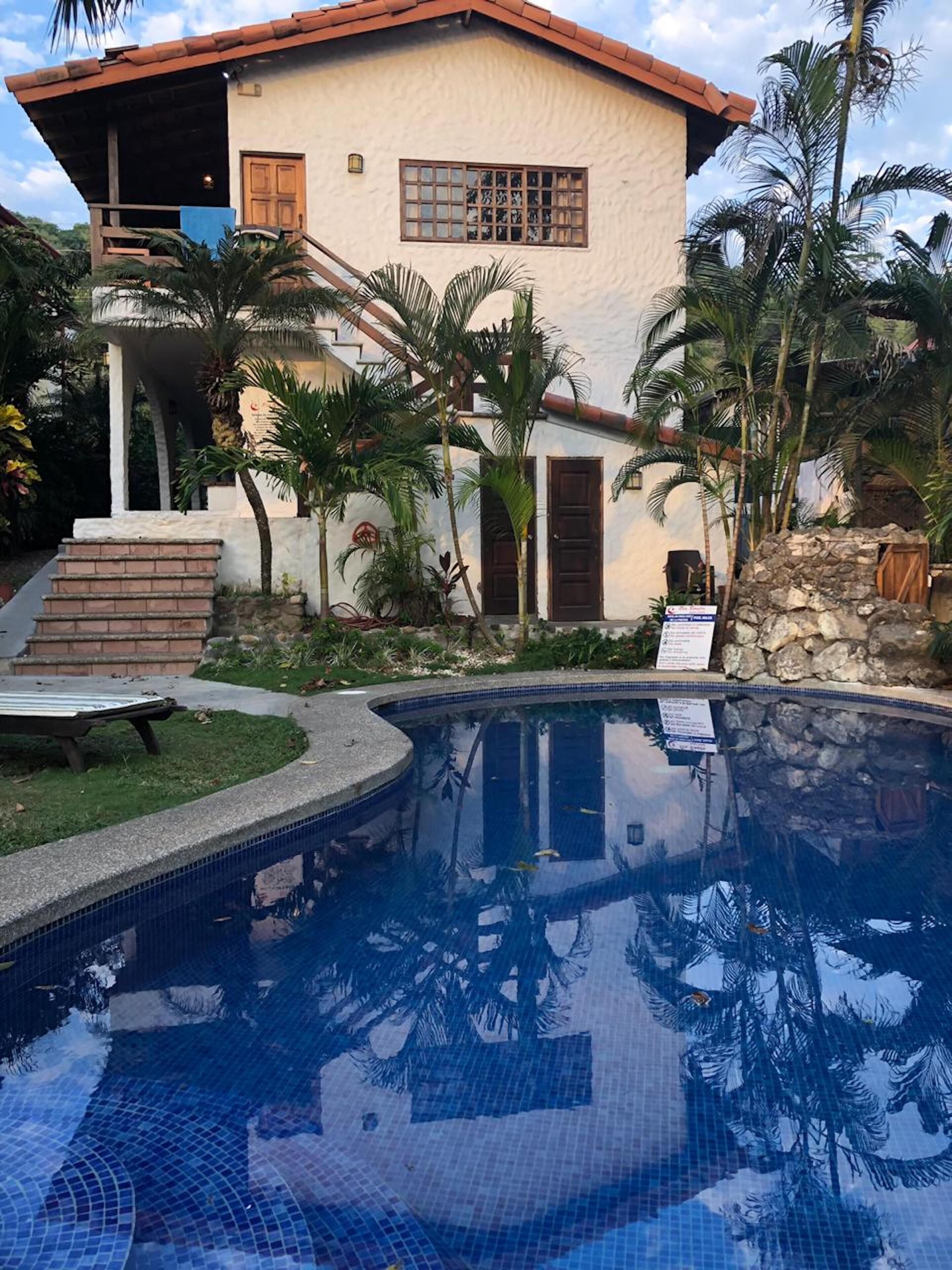A house with a swimming pool, surrounded by palm trees and a stone wall.