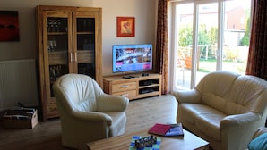 Uma sala de estar com dois sofás de couro, um aparador de madeira com portas de vidro, uma televisão e uma janela com cortinas.