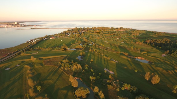 Vista aérea de um campo de golfe com vários buracos, corpos d'água e vegetação ao redor.