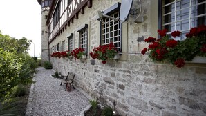 Un bâtiment en pierre doté d’une façade traditionnelle à colombages, d’un chemin de gravier et de pots de fleurs rouges.