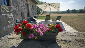 Un bâtiment en pierre doté d’un patio agrémenté d’un grand jardinier fleuri, de sièges extérieurs et offrant une vue sur la campagne.