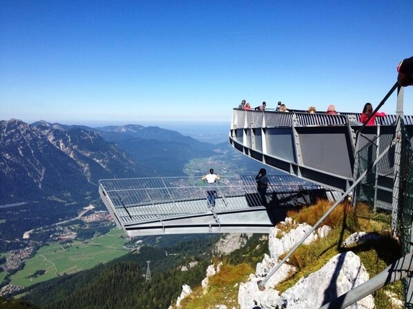 A glass bridge with a metal railing, overlooking a mountainous landscape with a valley below.