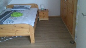 A bedroom with a sloped ceiling, a wooden bed, a nightstand, a wardrobe, and a small painting on the wall. - Good Morning! Welcome to East Frisia! (Berumbur)