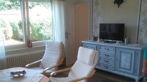 A room with two white armchairs, a small table with a metal tray, a television on a cabinet, and a window with curtains. - Good Morning! Welcome to East Frisia! (Berumbur)