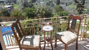 Un balcó amb dues cadires de fusta i una taula petita, amb vista a un paisatge idíl·lic ple d'arbres i una vista llunyana d'una vila.