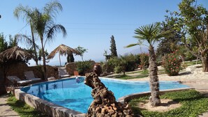 Una piscina amb un element central rocós, gandules i una estructura amb teulada de palla.