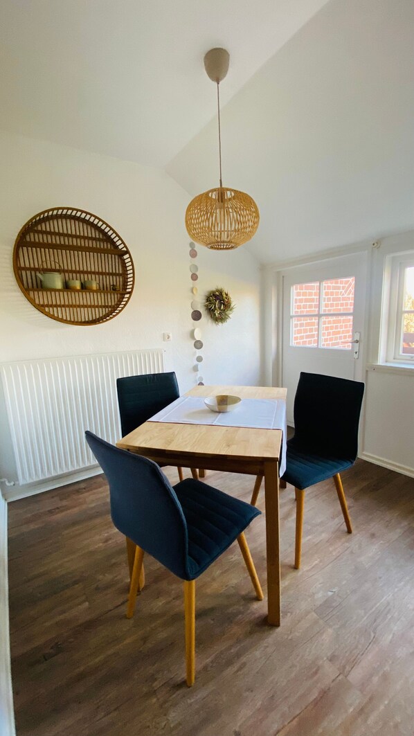 A dining area with a table, chairs, a hanging light fixture, a radiator, and a window with a view.