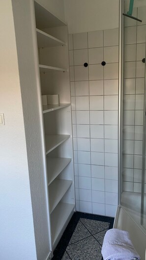 Un baño con paredes de azulejos blancos, cabina de ducha de vidrio y suelo de baldosas.